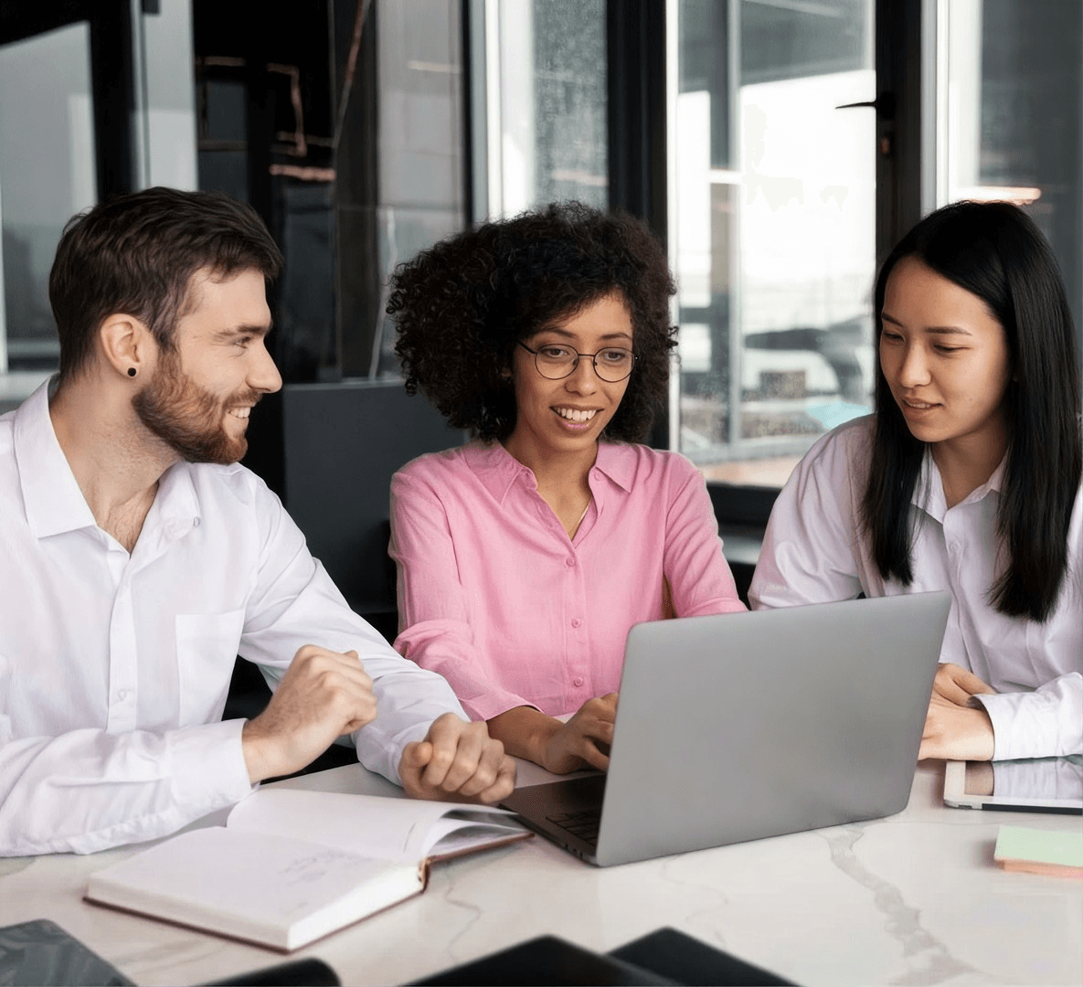 Três pessoas sorriem em volta de um notebook numa mesa de escritório.